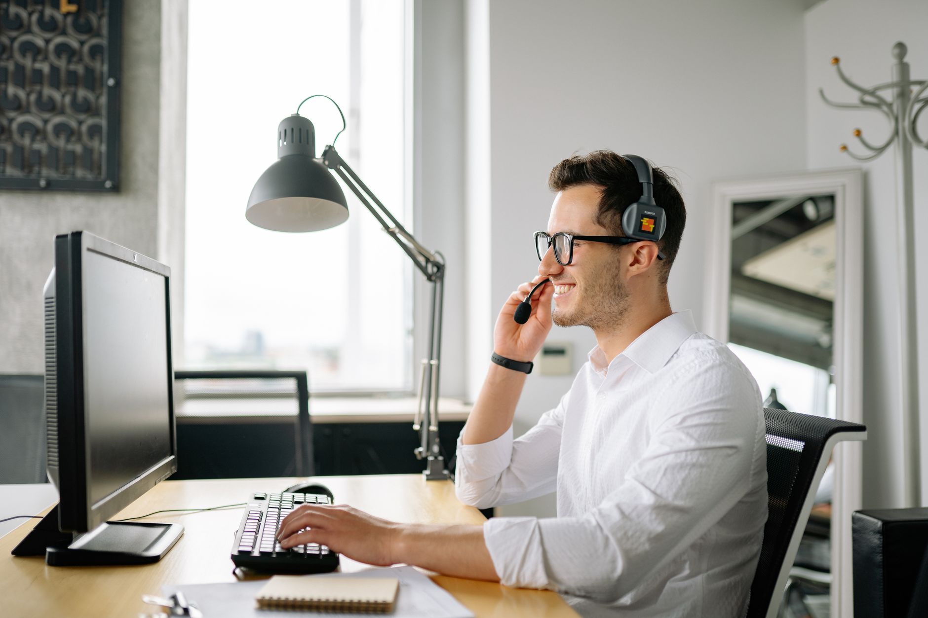 Smiling man wearing headset working at computer in bright office — illustrating: How to Choose a 5x5 VoIP Plan in Central Florida Without Overpaying on Hidden Setup Costs